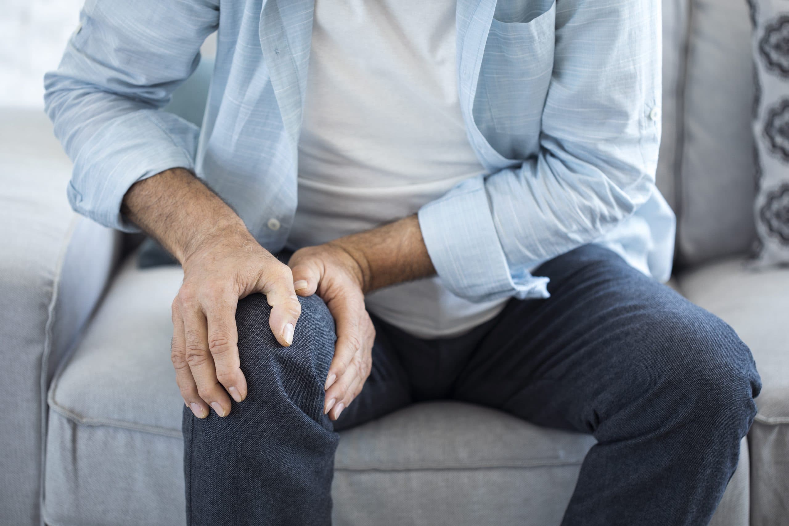 Man holding painful knee while seated on sofa